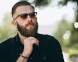 Mężczyzna z bujną brodą i okularami przeciwsłonecznymi, zastanawiający się, jak zapuszczać brodę.