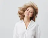 Uśmiechnięta dziewczyna z burzą blond włosów, które falują jak suche puszące się włosy.