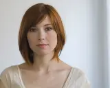 Kobieta z rudymi włosami w stylu krótki bob z grzywką na bok, patrzy wprost.