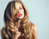 Kobieta z burzą falujących, blond włosów w stylu wolf cut, z wyrazistą czerwoną szminką.