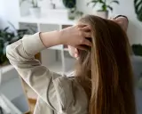 Dziewczyna delikatnie wplata palce we włosy, zastanawiając się, jak odżywić włosy. W tle lustro i rośliny.