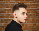 Młody mężczyzna z modną fryzurą, która dodaje mu uroku. To jedne z tych fryzur męskich, które odmładzają i podkreślają rysy twarzy.
