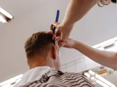 Fryzjerka precyzyjnie goli włosy przy uchu klienta, tworząc modny **undercut**.
