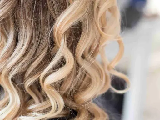 Falujące włosy z pasemkami blond z jasnym brązem, tworzące efekt słonecznych refleksów.