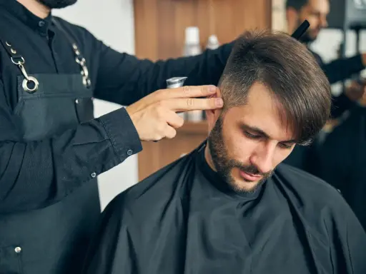 Fryzjer dopracowuje męskie fryzury z grzywką do przodu, tworząc stylowy look.