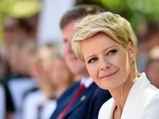 Kobieta z blond włosami w super krótkiej fryzurze damskiej, w białej marynarce, uśmiecha się.