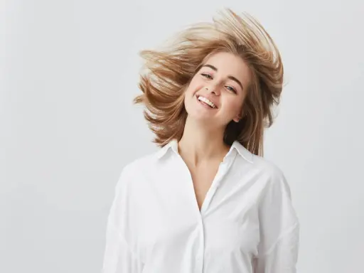 Uśmiechnięta dziewczyna z burzą blond włosów, które falują jak suche puszące się włosy.