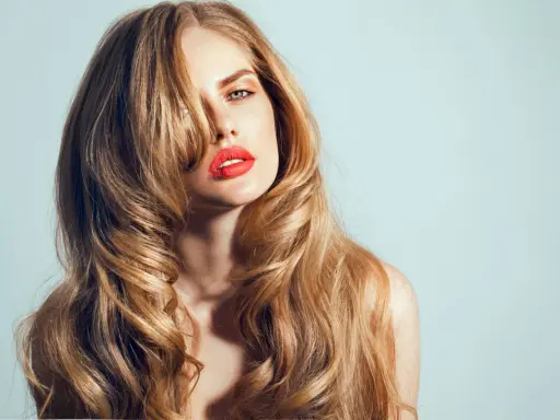 Kobieta z burzą falujących, blond włosów w stylu wolf cut, z wyrazistą czerwoną szminką.