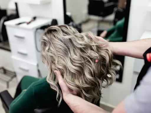 Profesjonalne usługi fryzjerskie: stylista układa falowane, blond włosy klientki w salonie.
