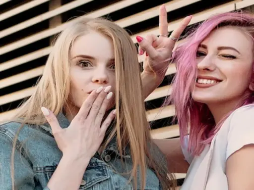 Dwie dziewczyny: jedna z bladą cerą i blond włosami, druga z różowymi włosami, robiące zdjęcie.