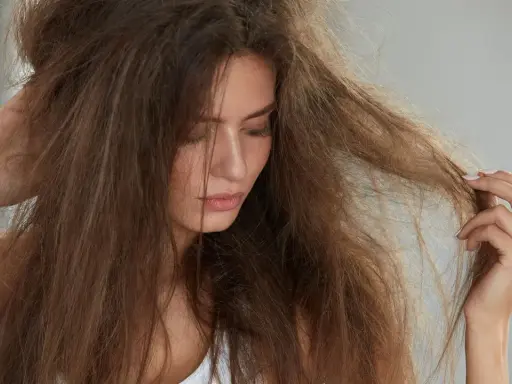 Kobieta zmartwiona swoimi **suchymi końcówkami włosów**, które są splątane i matowe.