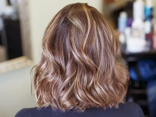 Piękne, falowane brązowe włosy z subtelnymi blond refleksami, które dodają im głębi i blasku.