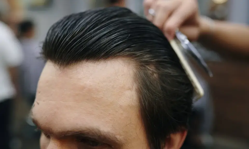 Fryzjer układa włosy mężczyzny na gładki slick back grzebieniem i nożyczkami.
