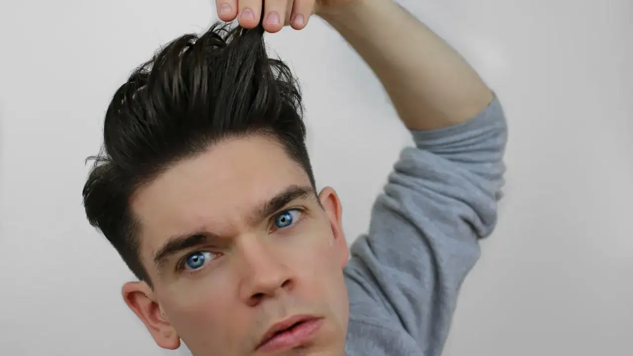 Chłopak z niebieskimi oczami poprawia swój messy quiff.