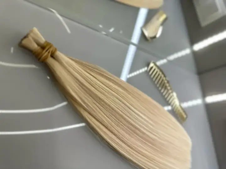 Pytasz, ile kosztuje przedłużanie włosów? Na zdjęciu widać pasma blond włosów gotowe do przedłużenia, obok złote grzebienie.
